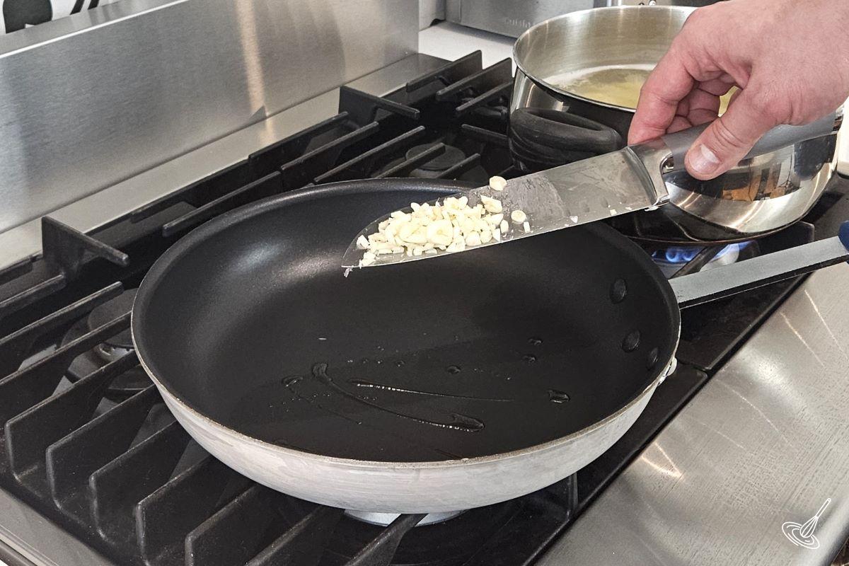 Someone placing minced garlic in a frying pan.
