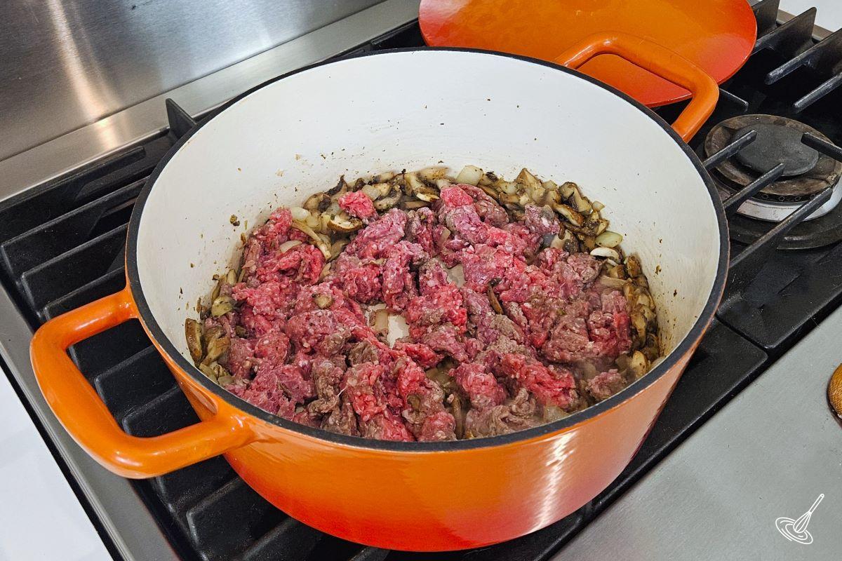 Ground beef cooking in a Dutch oven with vegetables.