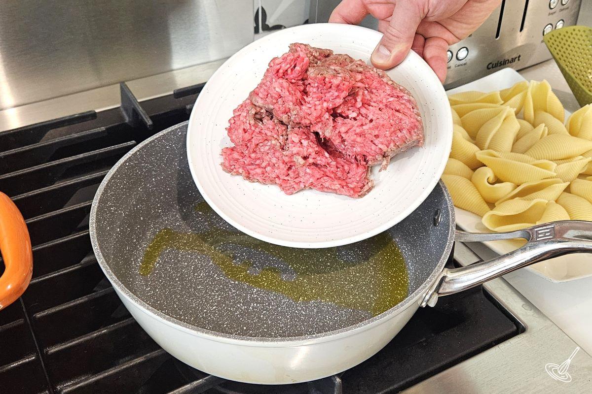 Someone placing ground beef in a large skillet.