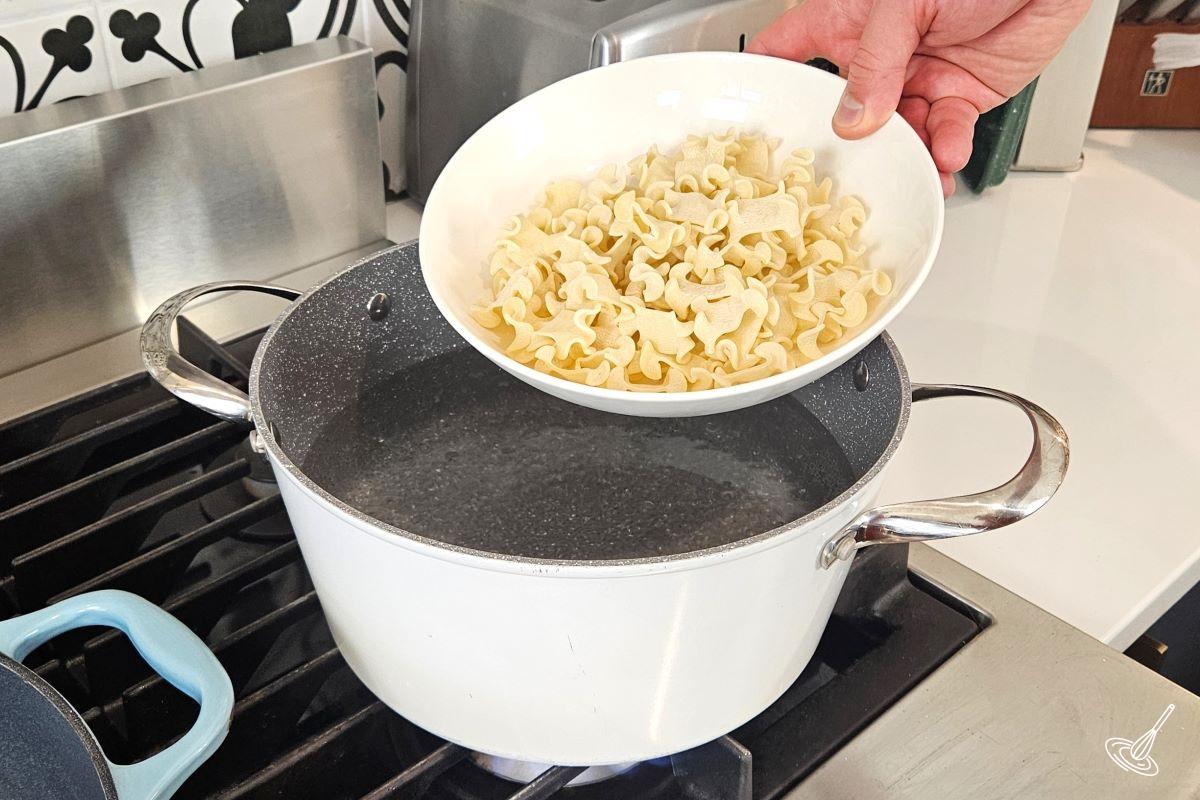 Someone placing a bowl of pasta in a large pot of boiling water.
