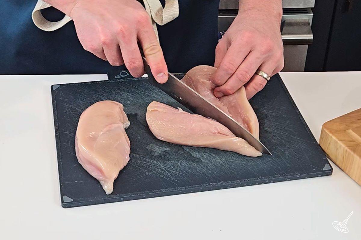 Someone cutting a chicken breast in half horizontally.