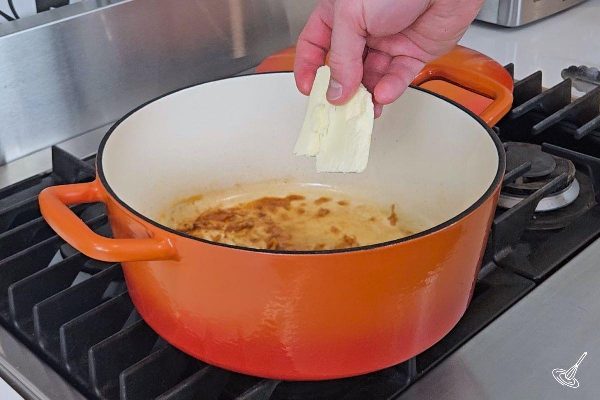 Someone placing butter into a Dutch oven. 