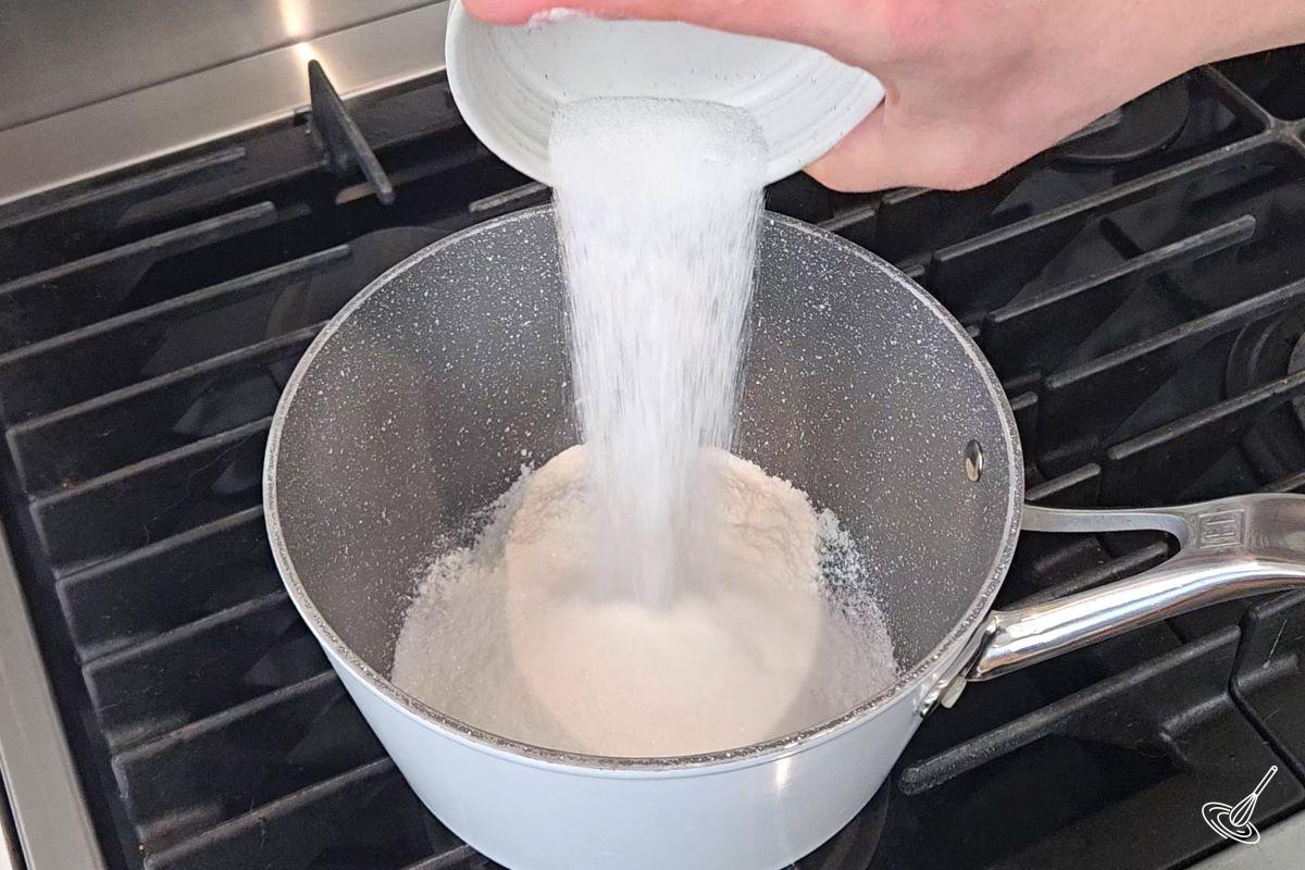 Someone pouring granulated sugar in a sauce pan. 