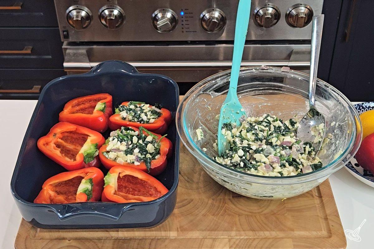 A bowl of spanakopita filling, beside a baking dish with bell pepper halves. 