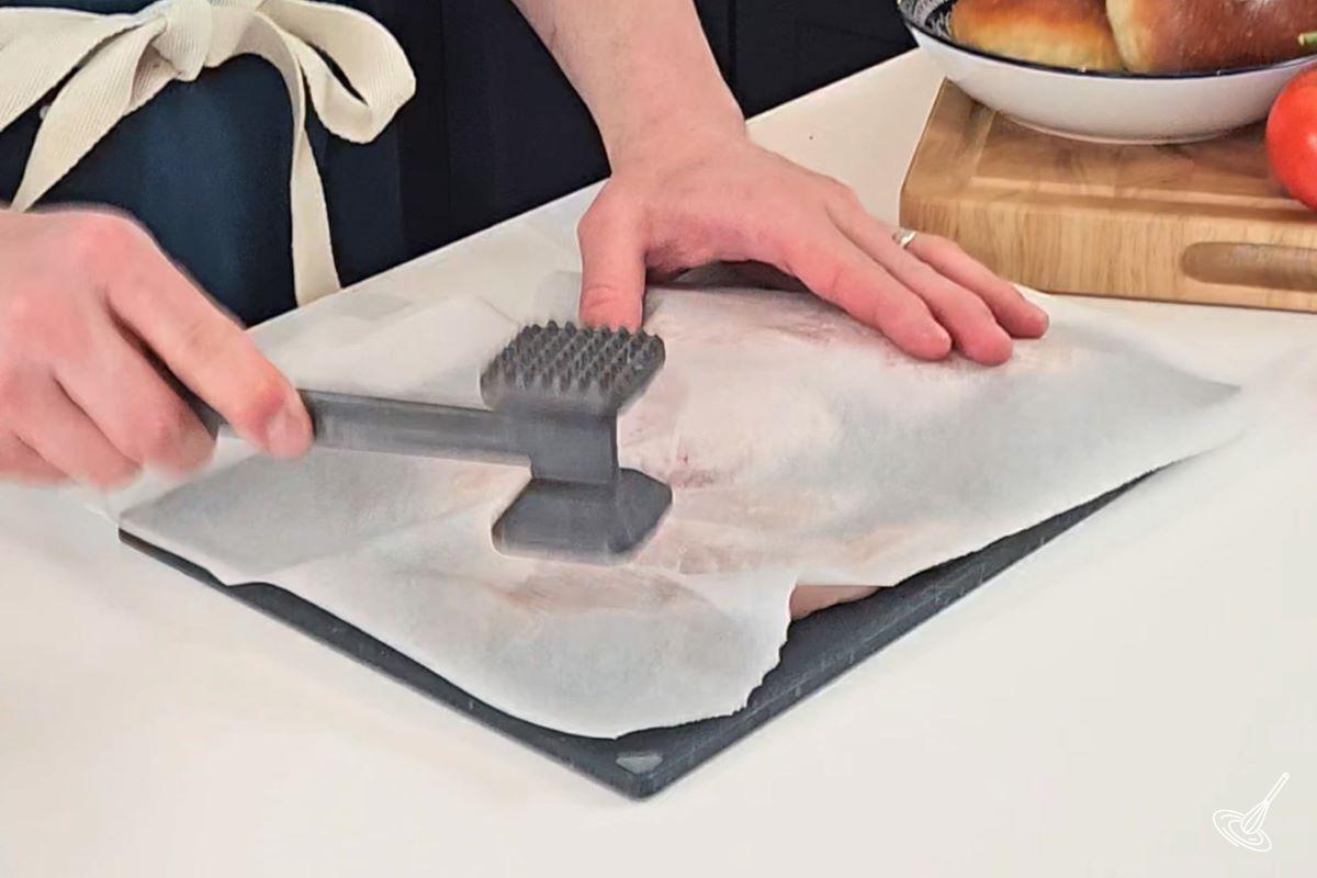 Someone using a meat tenderizer to flatten our chicken. 