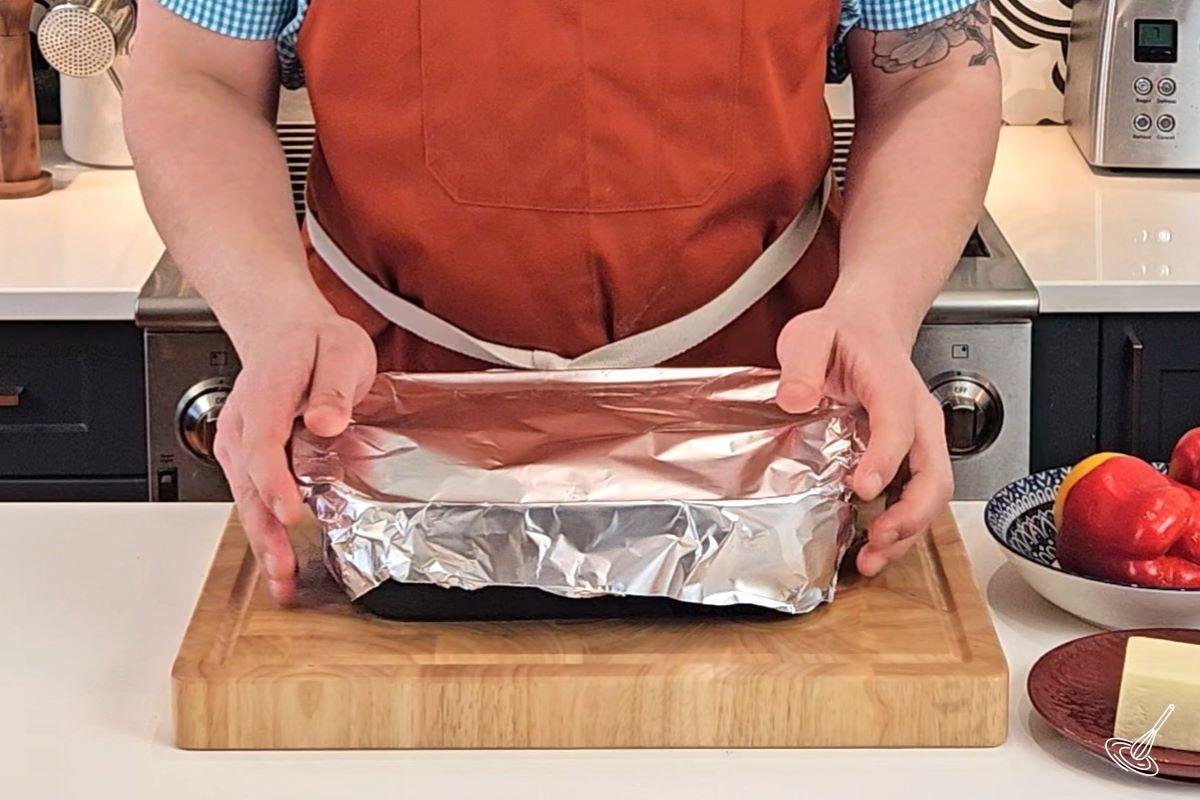 Someone placing foil over a baking dish.