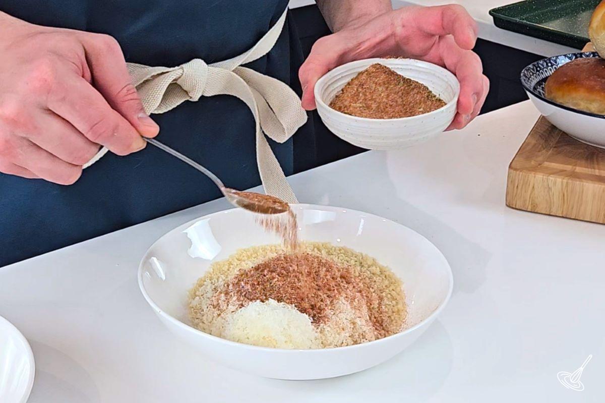 Someone sprinkle Cajun spice mix into a bowl with parmesan and panko crumbs.