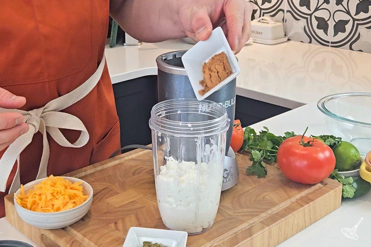Someone adding taco seasoning to a blender jar with cottage cheese.