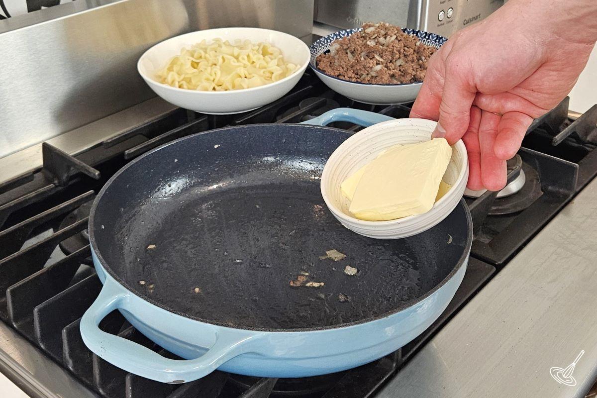 Someone placing butter in an empty skillet. 