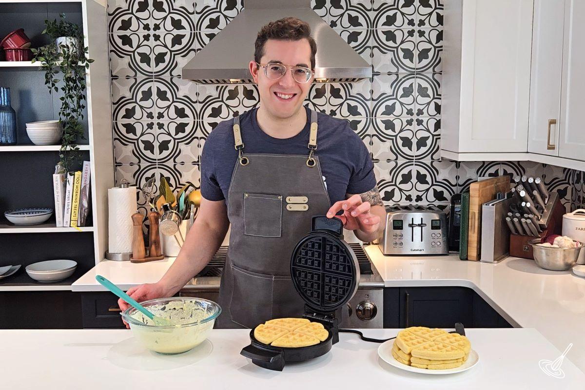 Someone standing behind a kitchen counter and making waffles. 