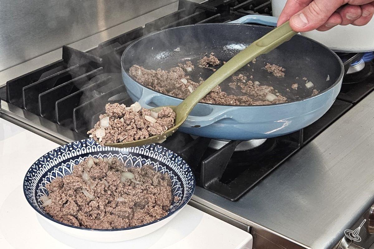 Someone transferring cooked ground beef from a skillet to a bowl.  