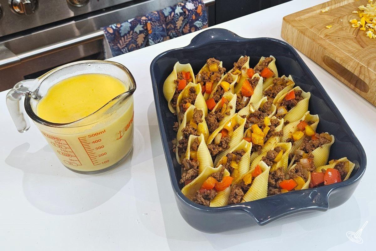 A pan of Philly Cheesesteak Stuffed Shells with a side of cheese sauce.