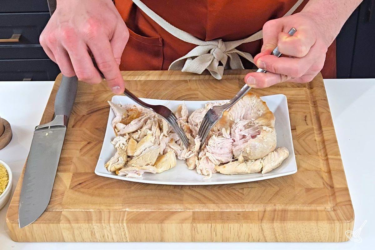 Someone using two forks to shred cooked chicken breasts.