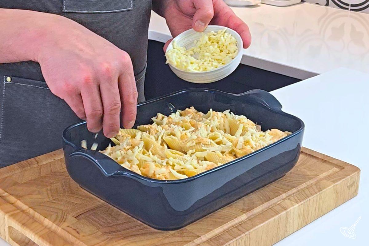 Someone sprinkling grated cheese on top of stuffed jumbo pasta shells.