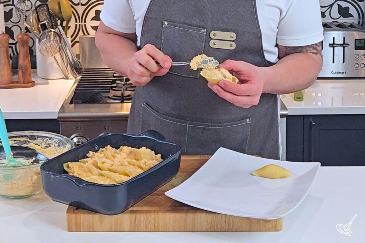 Someone stuffing jumbo pasta shells with a buffalo chicken cream cheese mixture. 