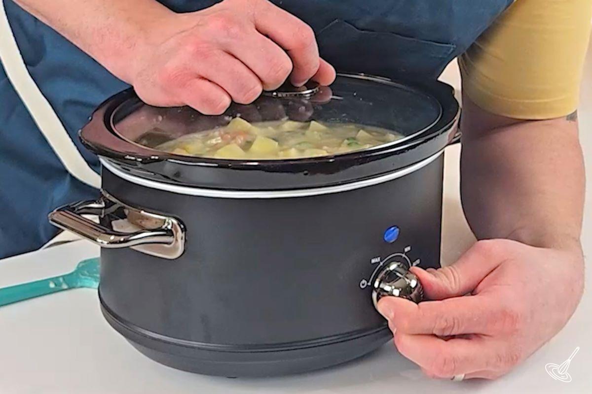Someone placing the lid on a slow cooker and turn the heat to the maximum setting. 