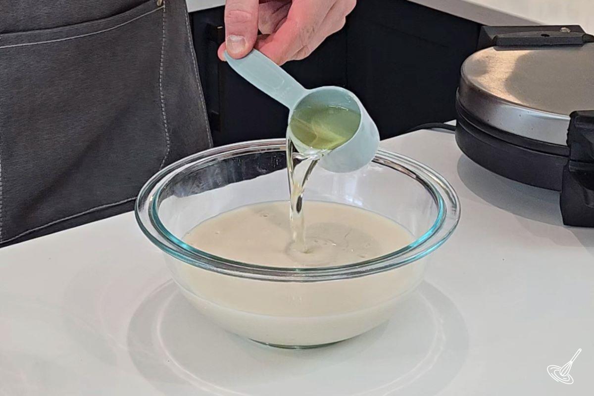 Someone adding canola oil to a bowl of milk with eggs. 