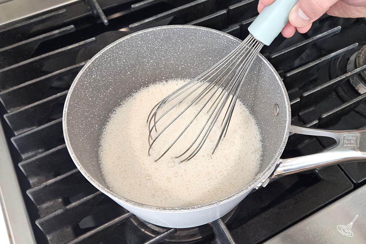 Someone whisking a milk mixture in a saucepan.