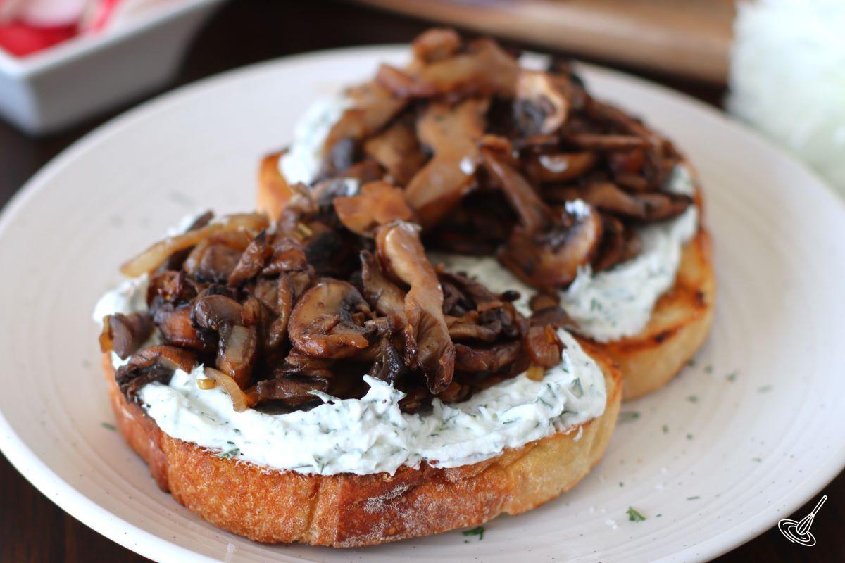 Sliced of bread topped with a goat cheese mixture and a fried mushroom mixture.