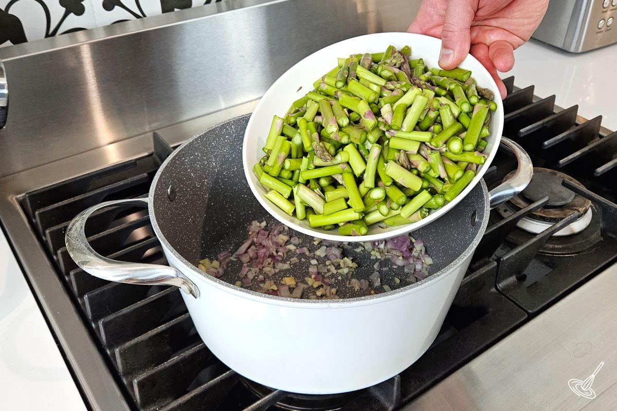 Someone adding chopped asparagus to a soup pot.