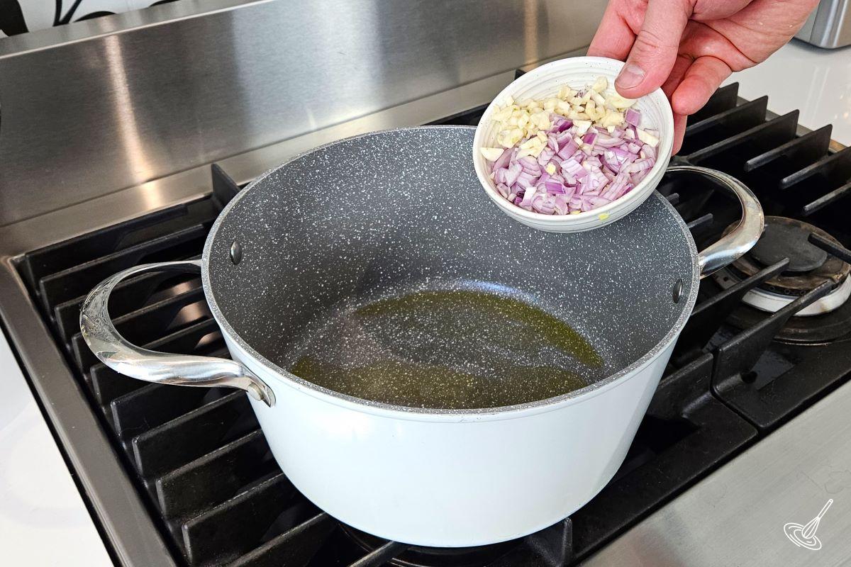 Someone placing chopped garlic and shallots in a large soup pot on the stove. 