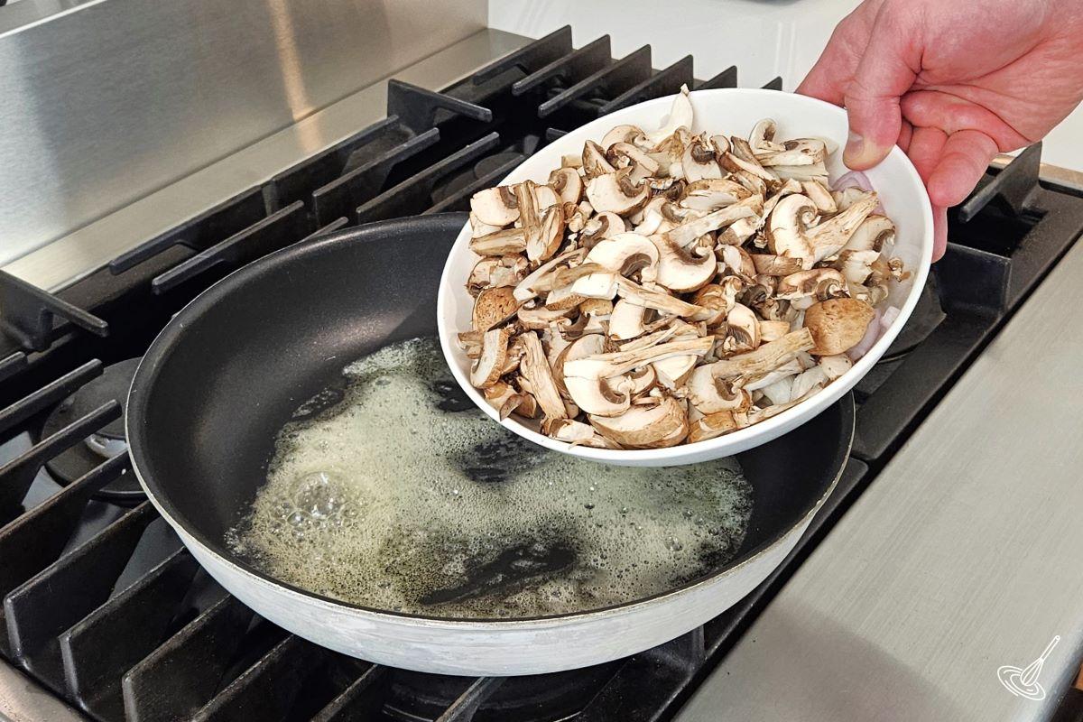 Someone placing mushrooms in a frying pan with butter.