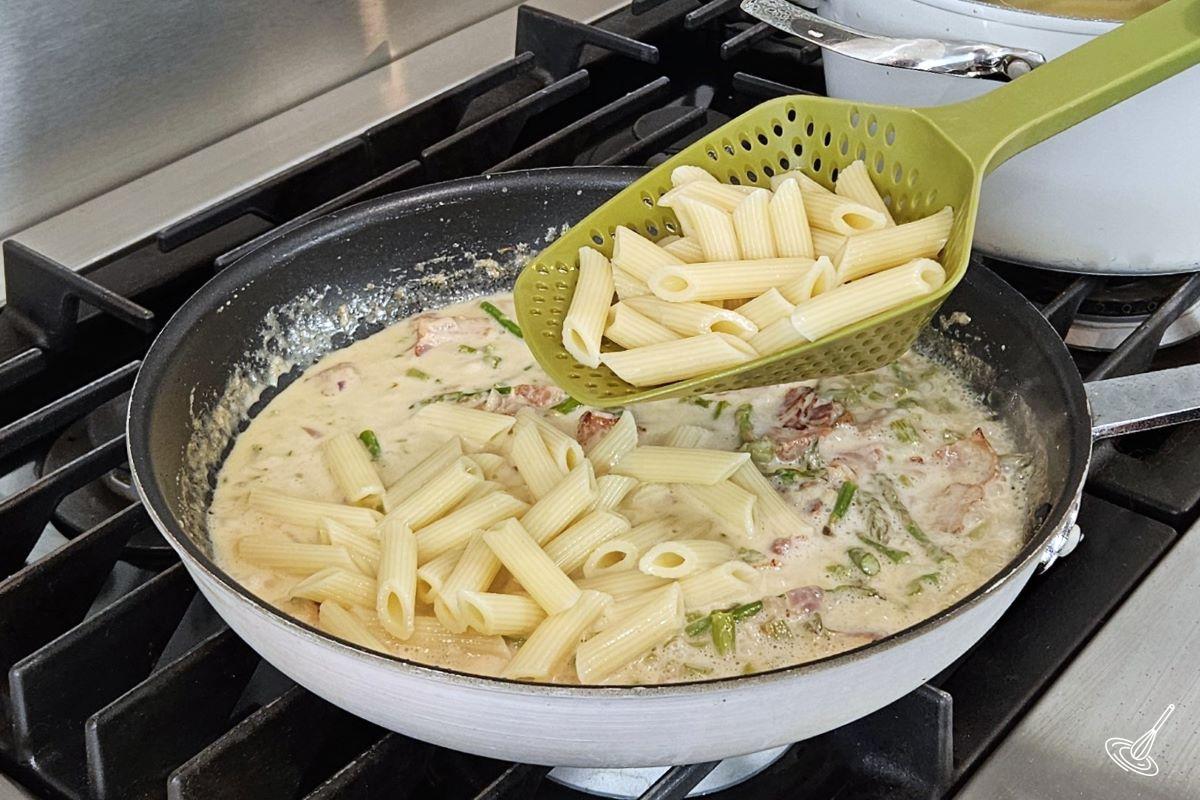Someone adding cooked pasta a creamy sauce in a pan. 