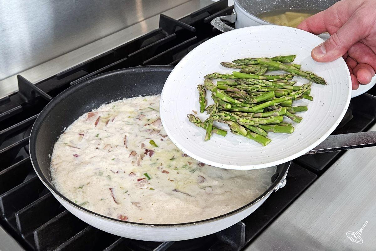 Someone placing asparagus tips in a frying pan containing a cream sauce.