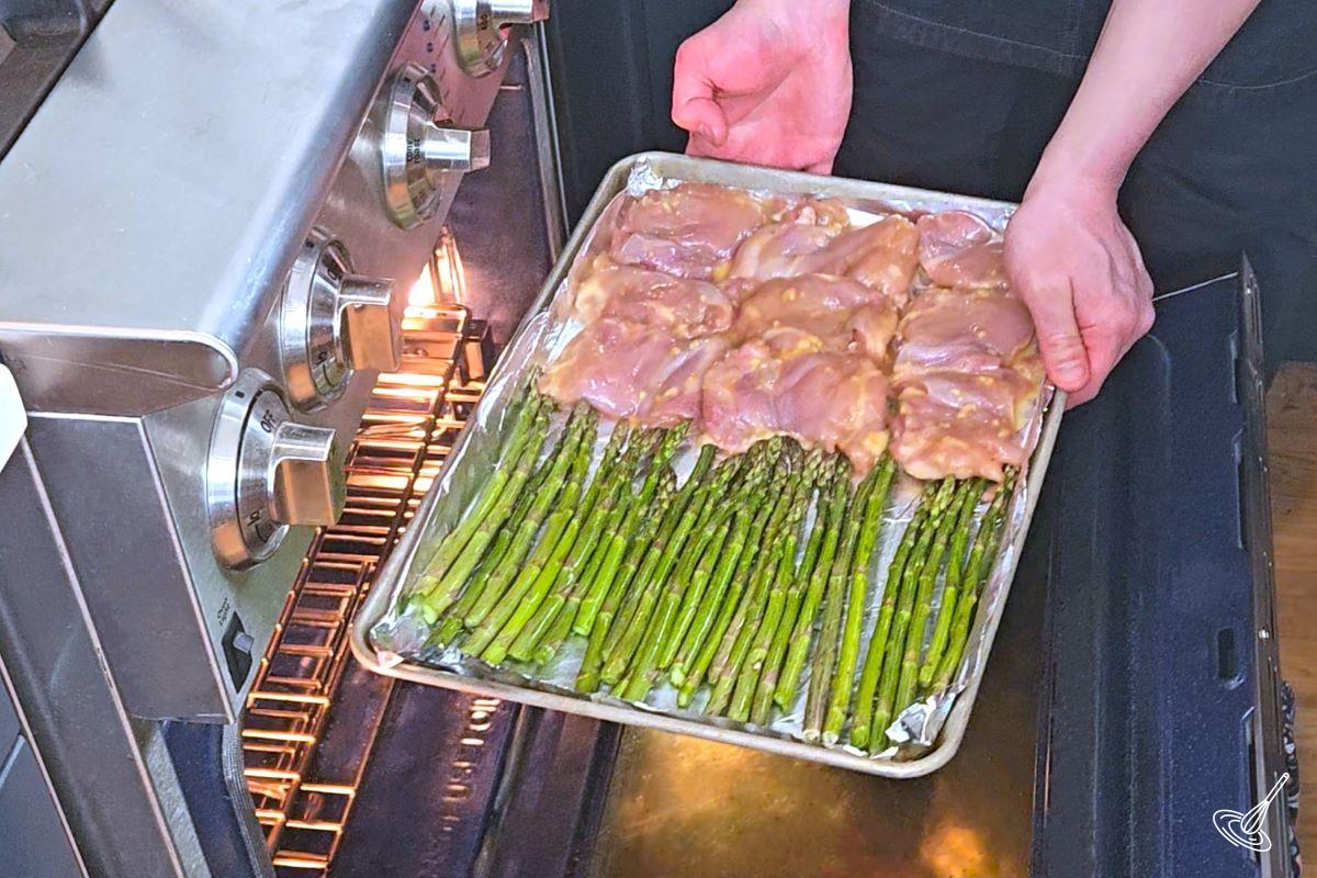Someone placing a sheet pan miso honey chicken into the oven.