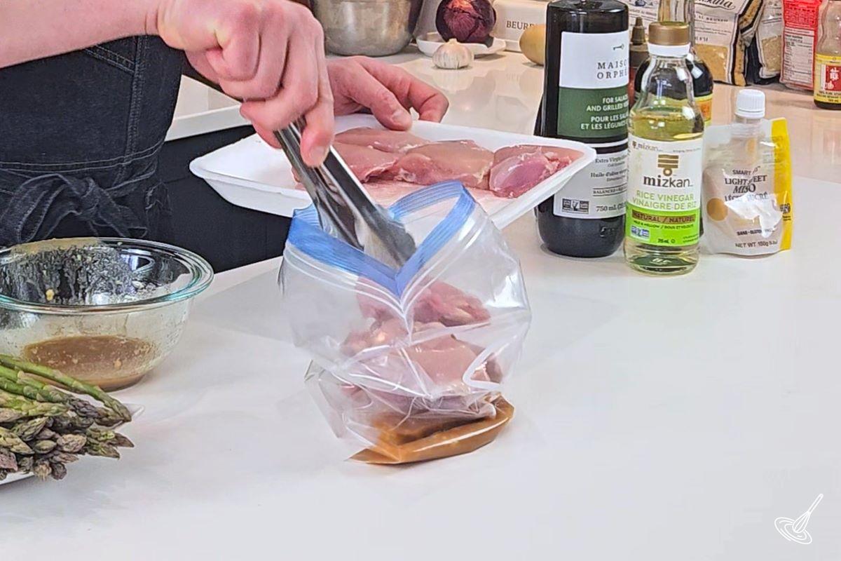 Someone placing chicken thighs in a sealable plastic bag with marinade. 