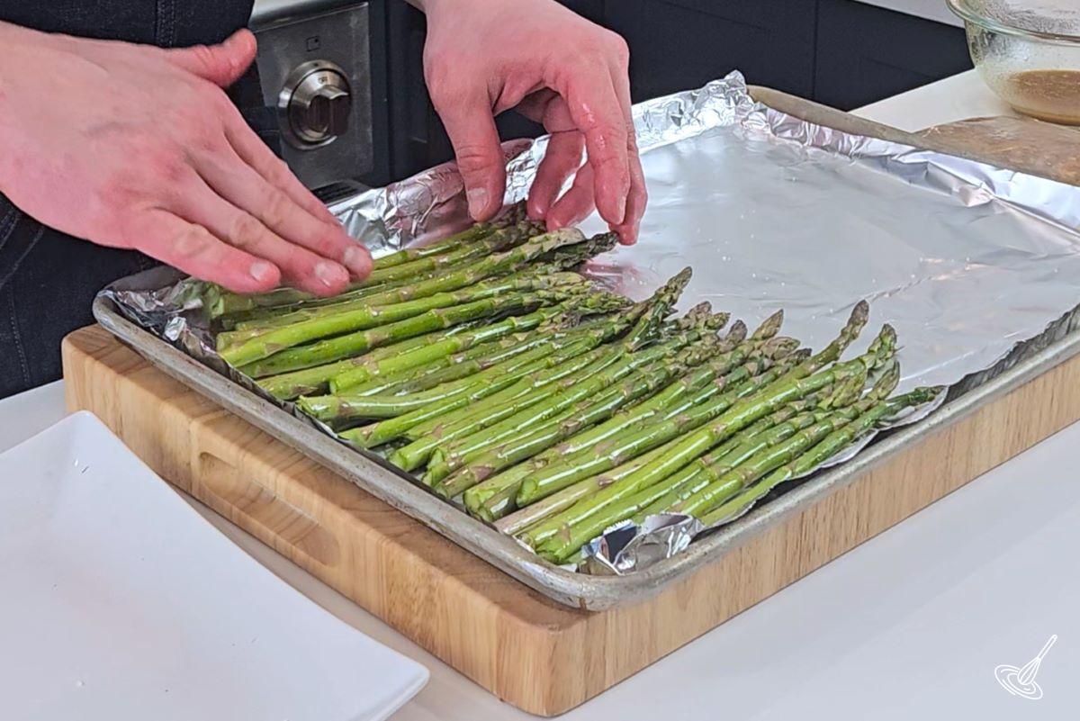Someone placing asparagus on a sheet pan which is lined with aluminum foil.