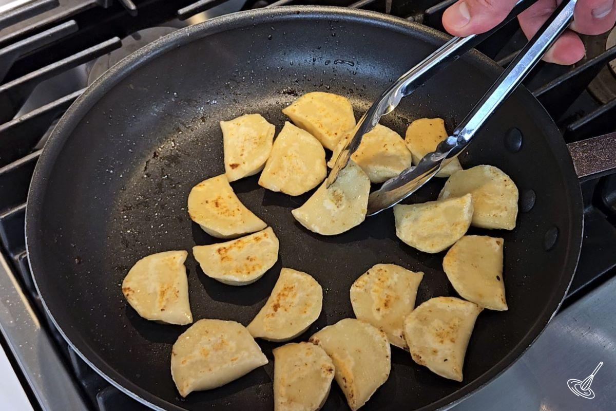 Pierogies cooking in a large frying pan.