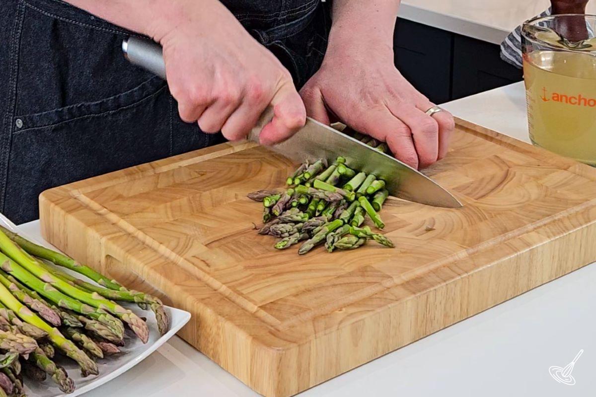 Someone chopping up asparagus on a wooden cutting board.
