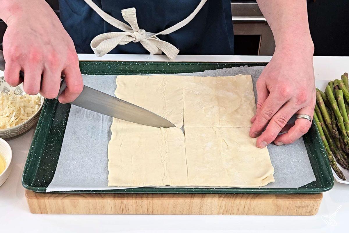 Someone cutting a piece of puff pastry in four squares. 