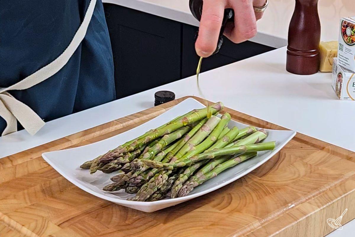 Someone drizzling olive oil on a stack of asparagus. 