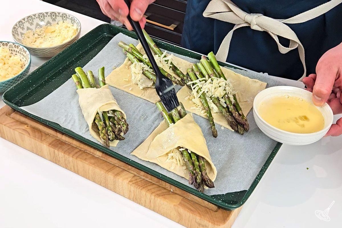 Someone brushing egg wash on top of Alfredo Asparagus Bundles. 