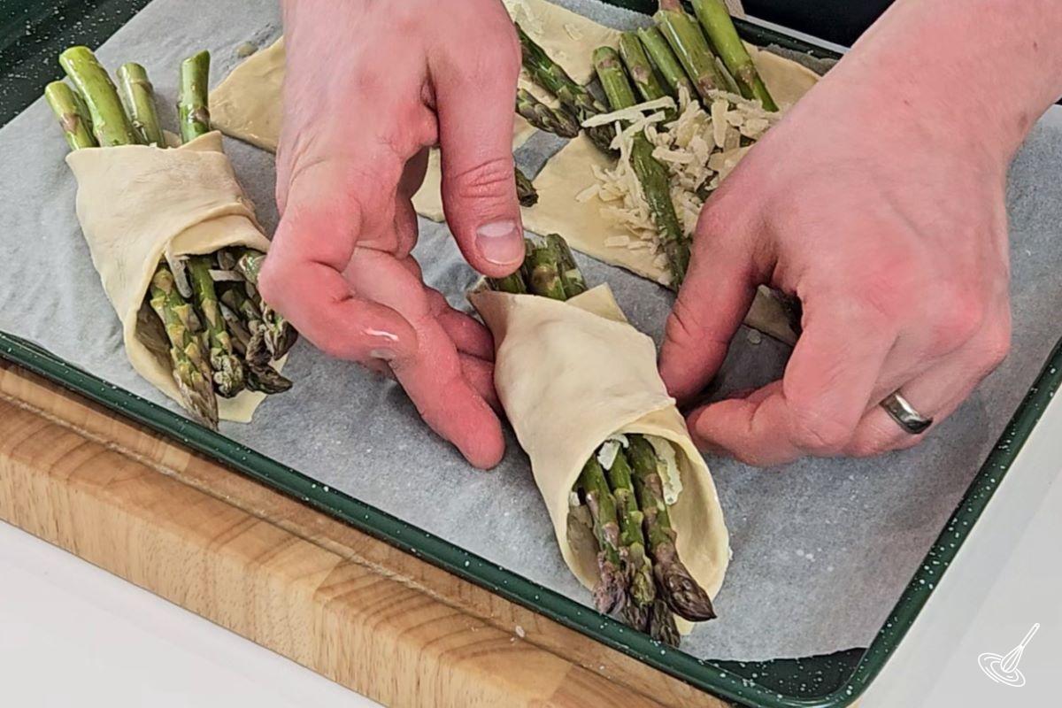 Someone wrapping a bundle of asparagus with puff pastry. 