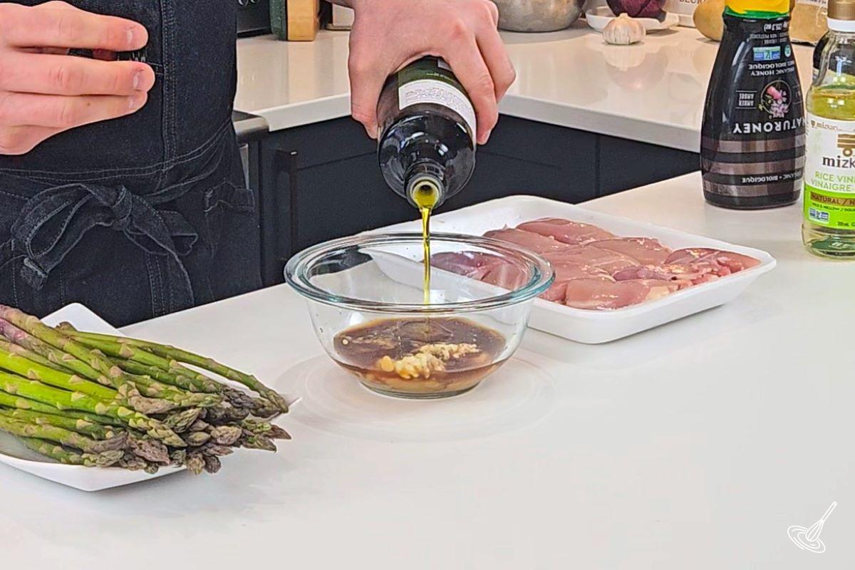 Someone pouring oil in a small bowl to make the Miso Honey Chicken marinade.