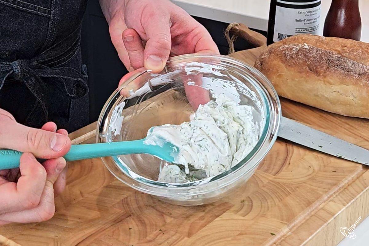 Someone stirring a herb cheese mixture in a small bowl. 