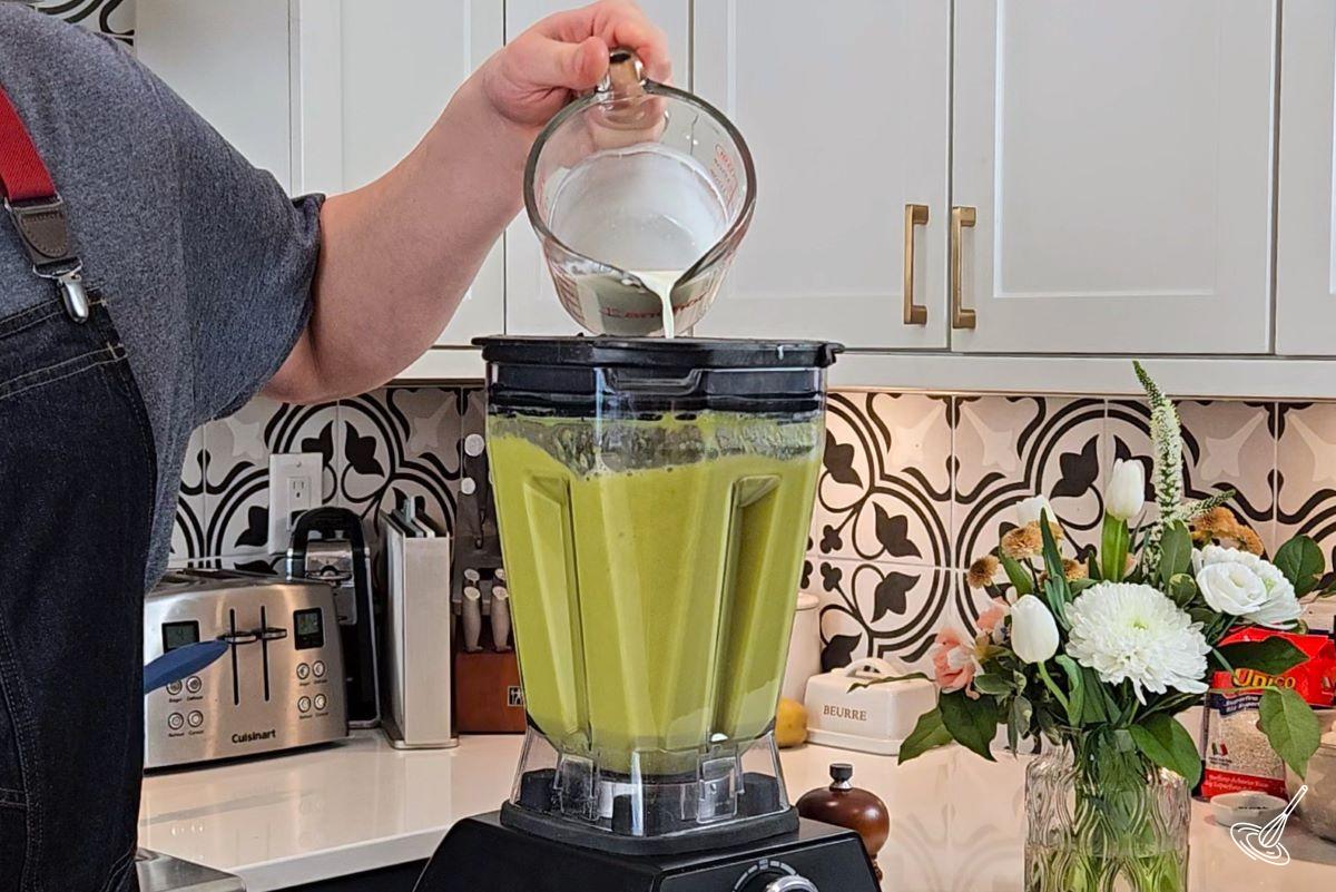 Someone pouring in cream into a blender with soup.
