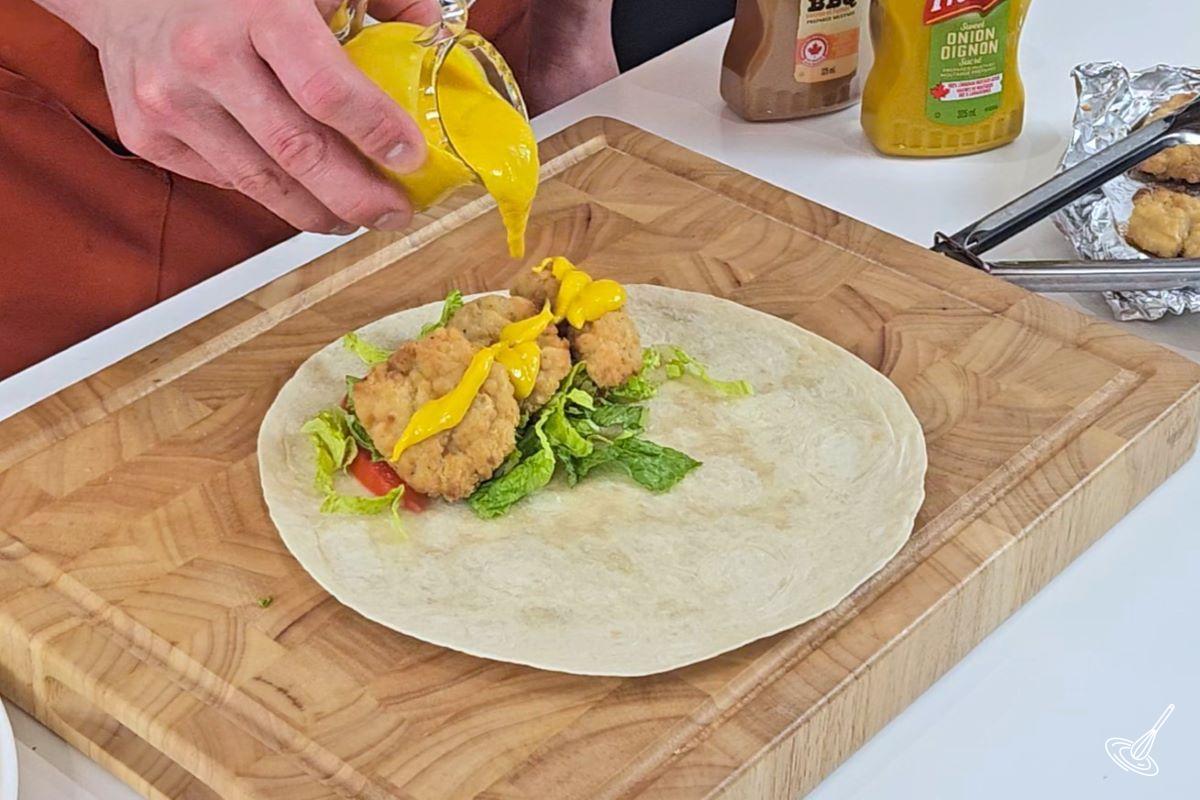 Someone pouring honey mustard on top of chicken tender in a wrap. 
