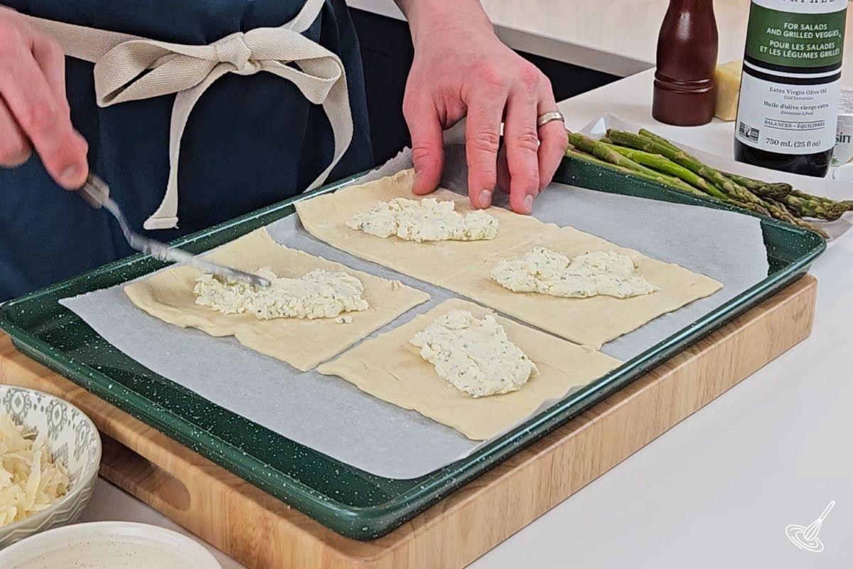 Someone spreading cheese on top of squares of puff pastry.