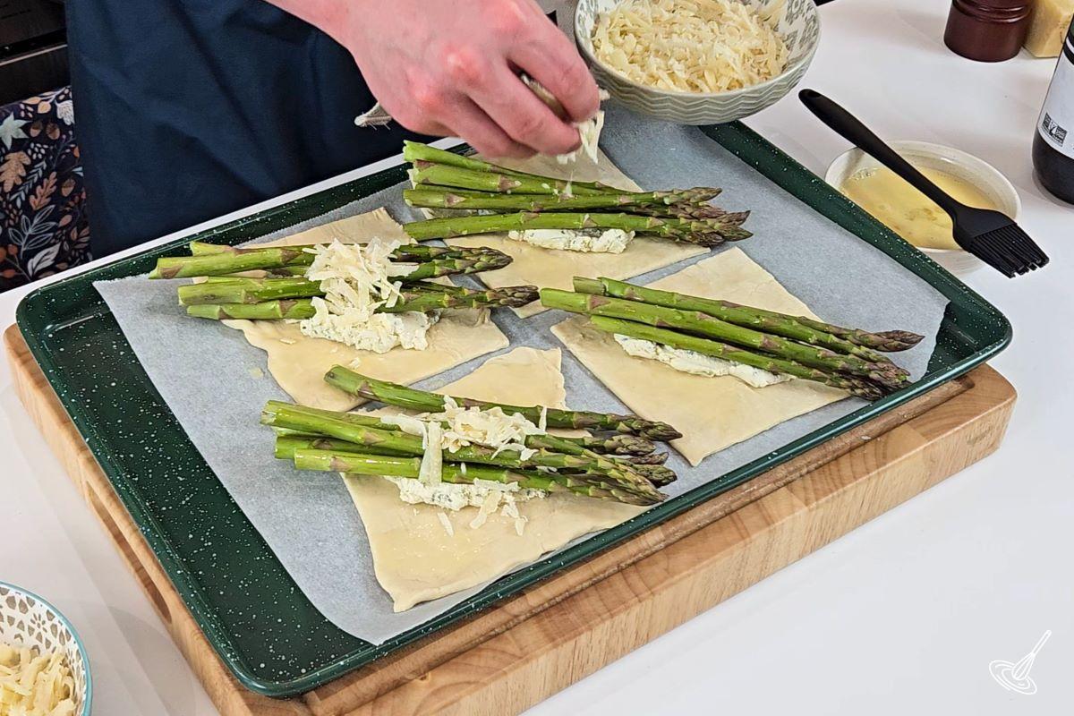 Someone sprinkling cheese on top of asparagus bundles. 