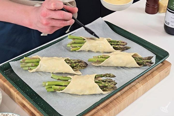 Someone brushing Alfredo Asparagus Bundles with egg wash.