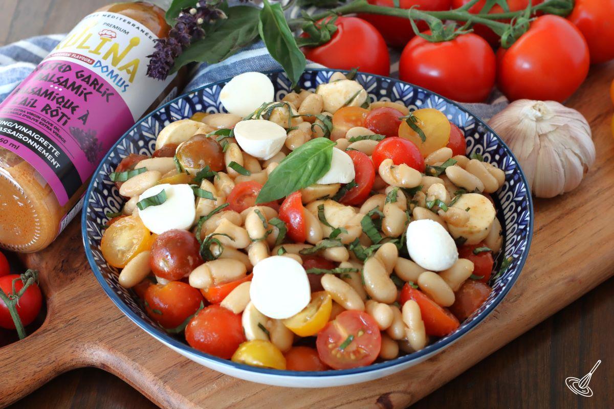 White Bean Caprese Salad in a serving bowl with a bottle of salad dressing on the side.