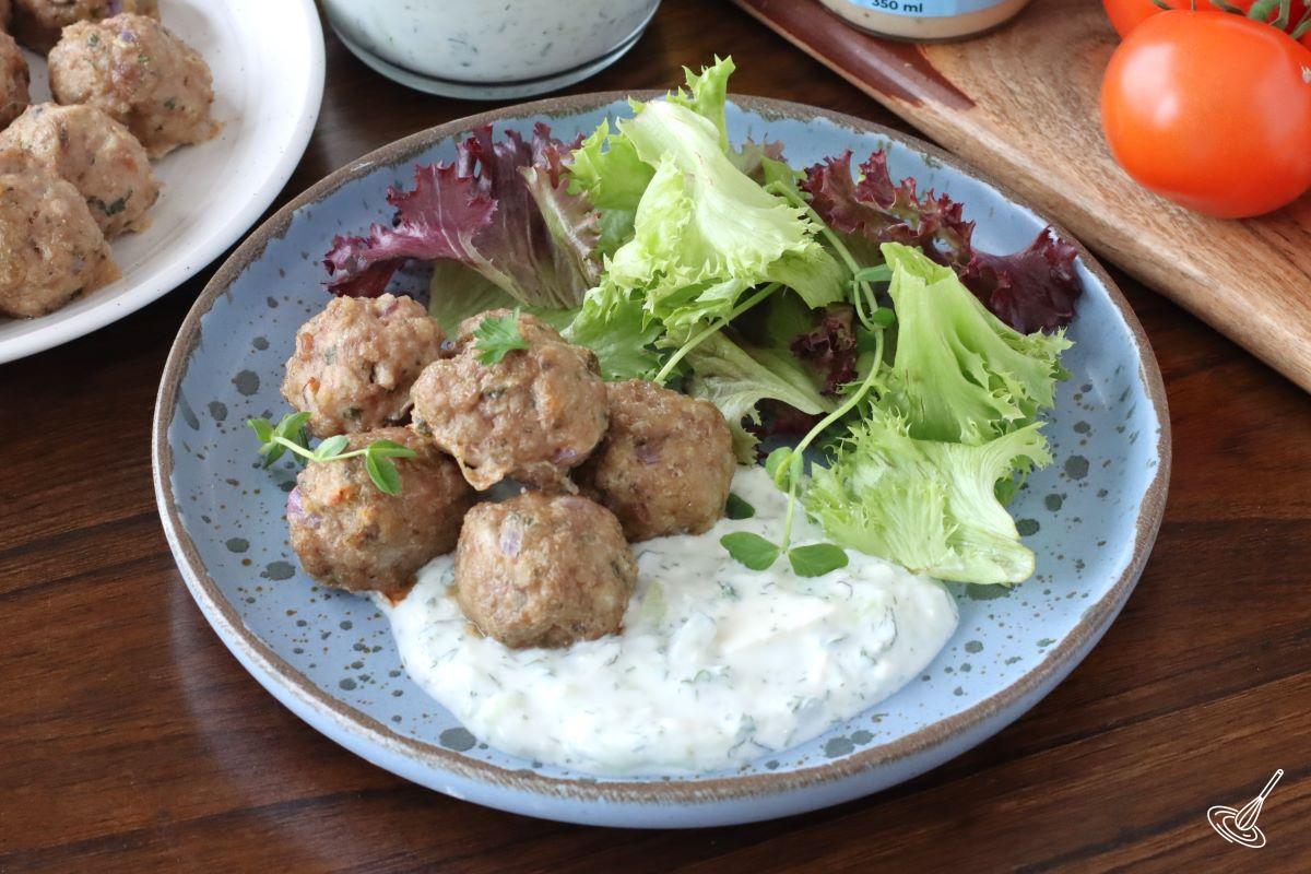 Greek Lamb Meatballs on a plate with mixed greens and a tzatziki sauce. 