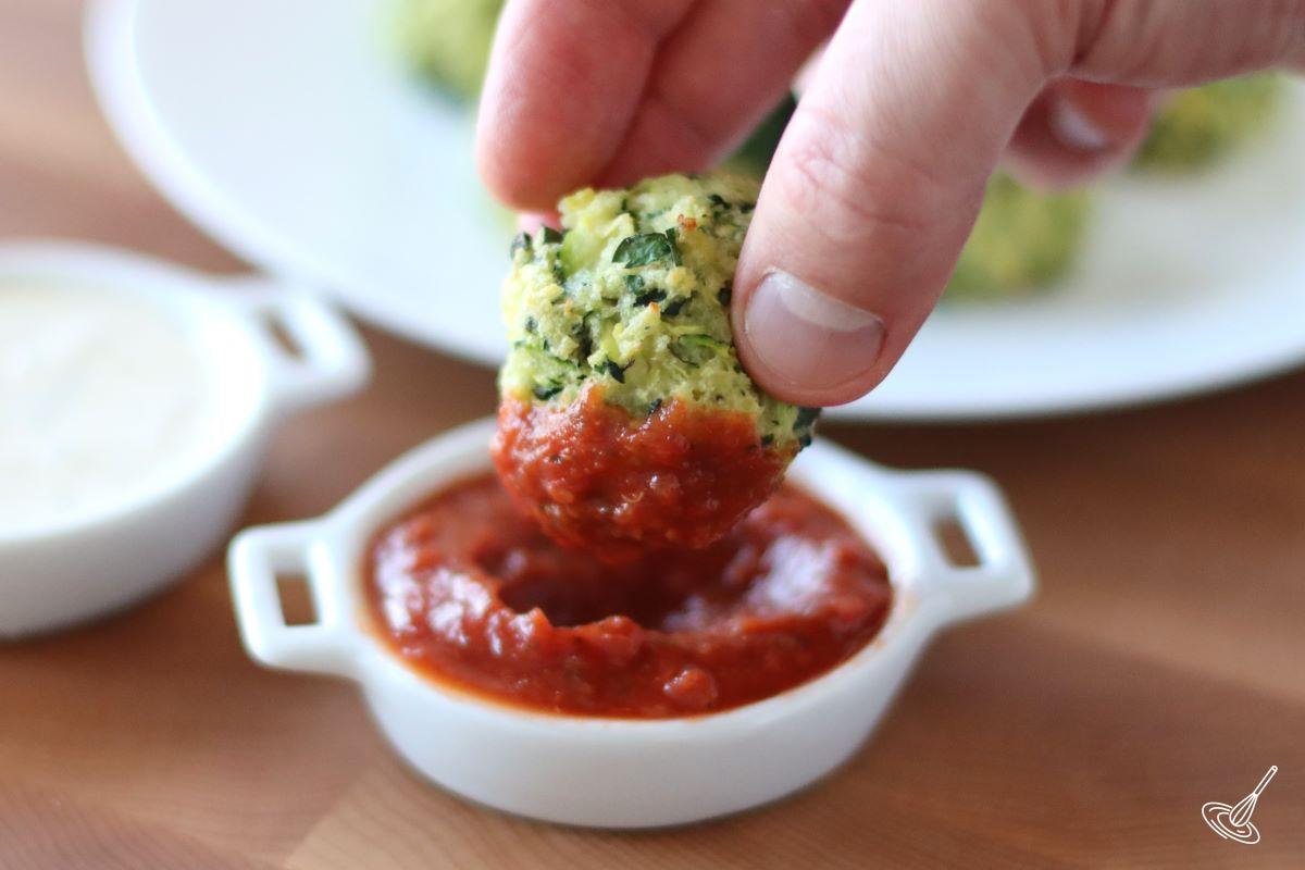 Someone dunking a zucchini garlic bite into marinara sauce. 