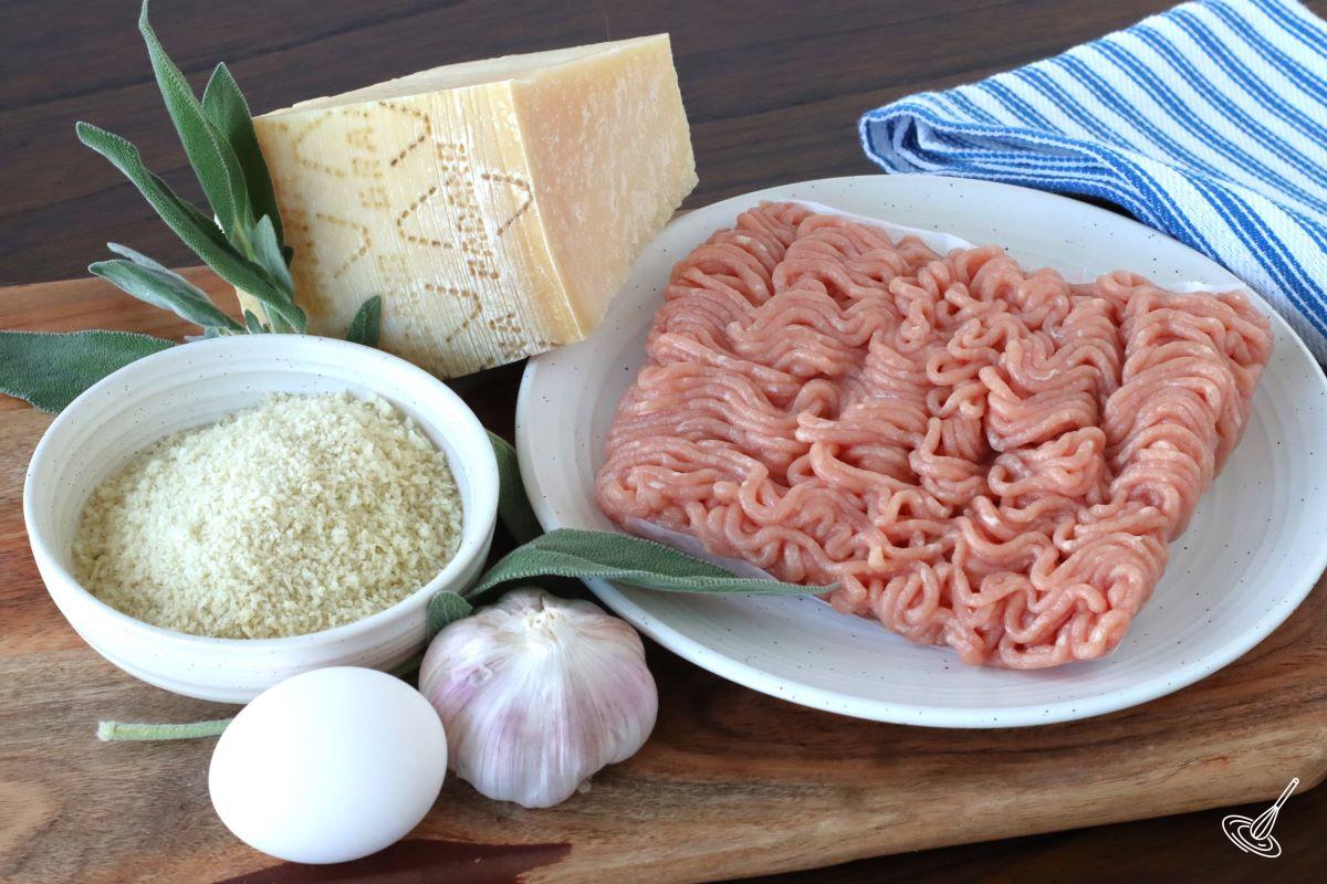 Ingredients on a cutting board, including panko crumbs, egg, ground chicken, fresh sage and parmesan.