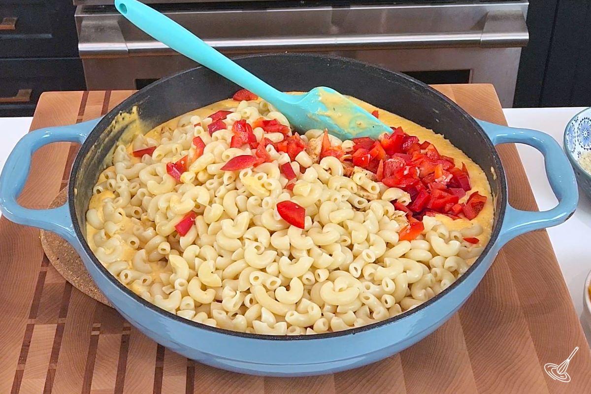 A large skillet containing cheese sauce, cooked chicken, cooked pasta and chopped bell pepper.