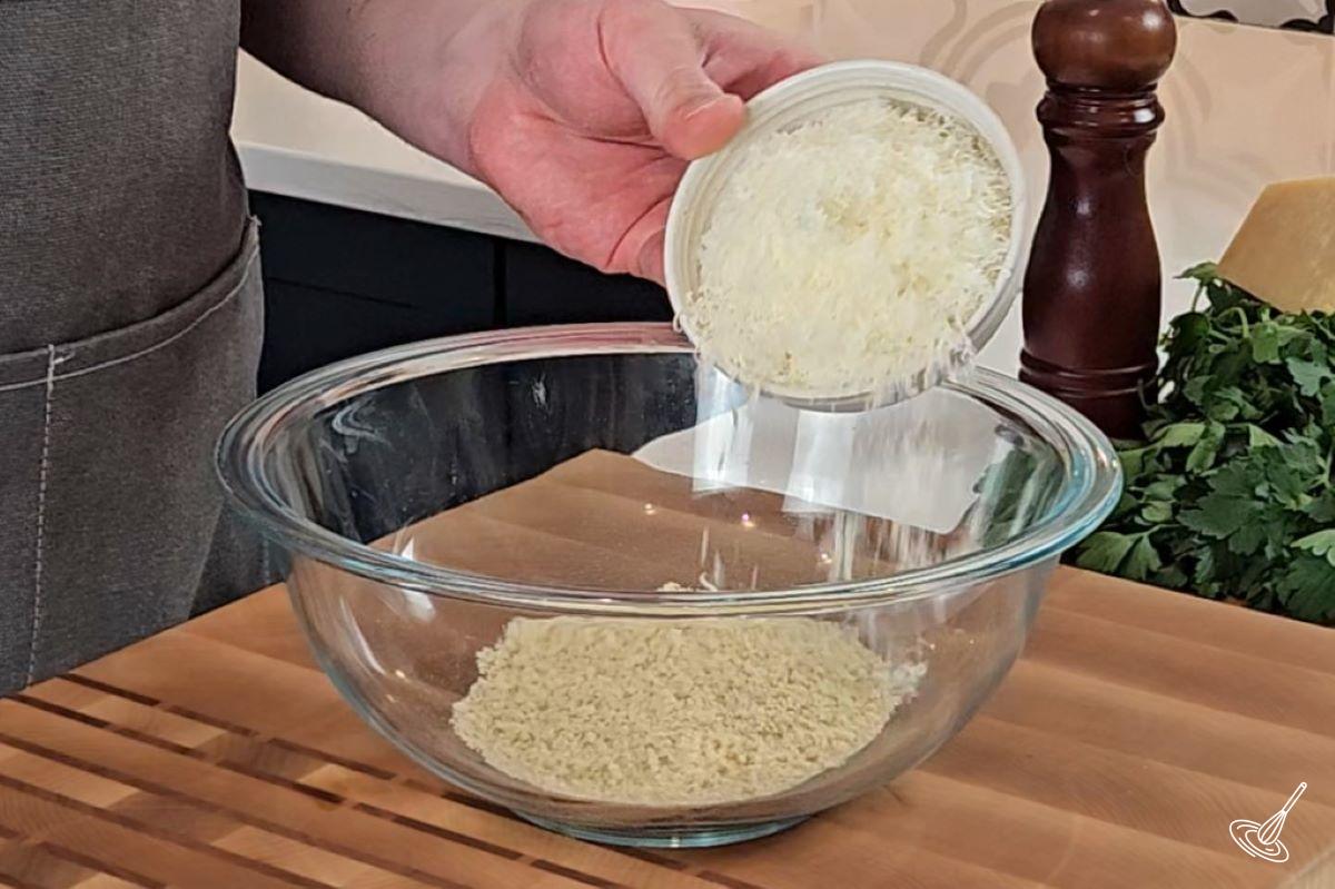 Someone putting grated parmesan into a large bowl with panko crumbs. 